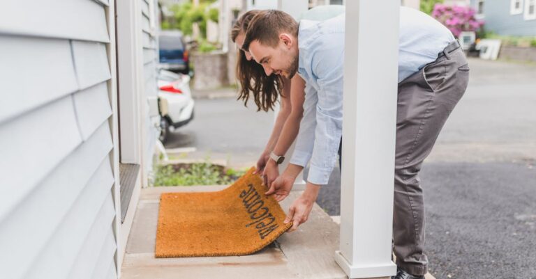A young couple setting up a welcome mat on the porch of their new home, symbolizing new beginnings.